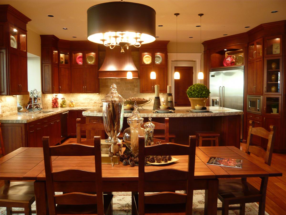 Elegant kitchen and dining area with wooden cabinets, a large dining table, modern pendant lights, stainless steel appliances, and decorative jars and plants on the counters and table.