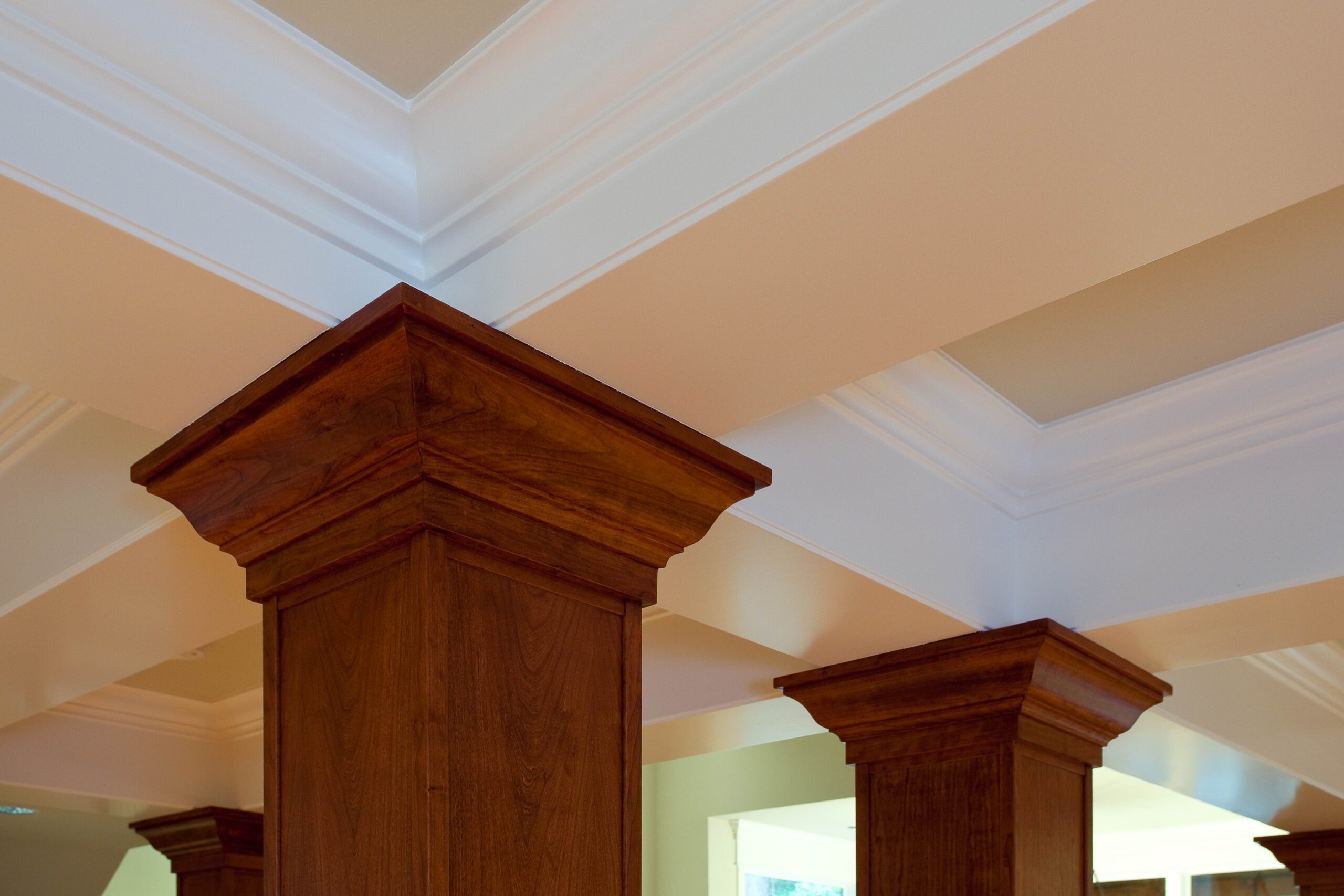 Wooden columns with detailed crowns support a coffered ceiling painted white, creating an elegant architectural feature in a well-lit interior space.